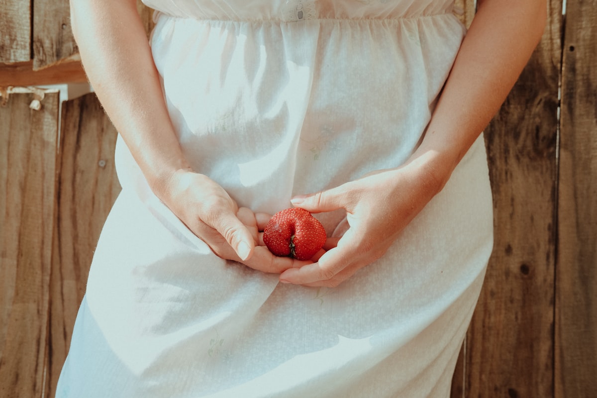 Grávida a segurar um morango junto à barriga, vestido branco